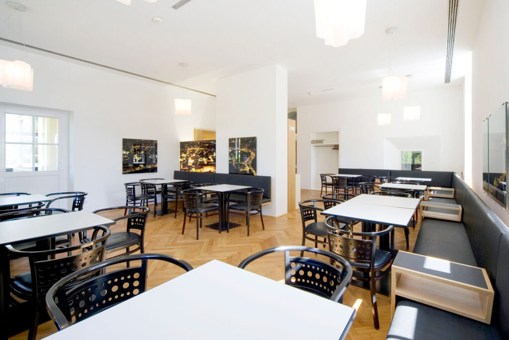 Heller Speiseraum mit weißen Tischen und schwarzen Stühlen.