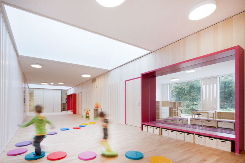 Helle Kita mit bunten Spielpunkten am Boden und spielenden Kindern in Bewegung.