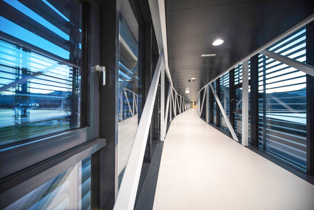 Moderner verglaster Verbindungsgang mit klaren Linien und Stahlträgern.