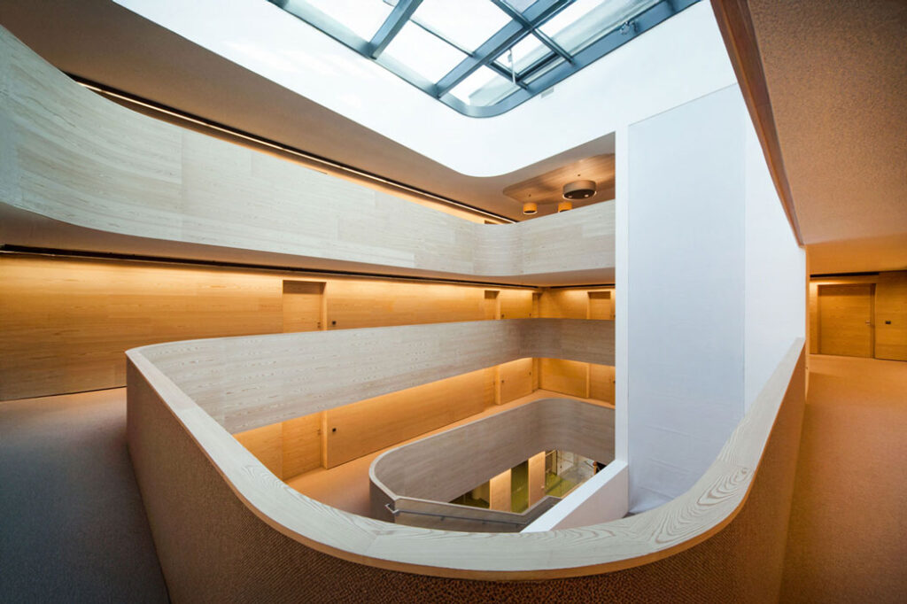 Innenansicht eines modernen mehrgeschossigen Atriums mit Lichtdecke und geschwungenen Linien.