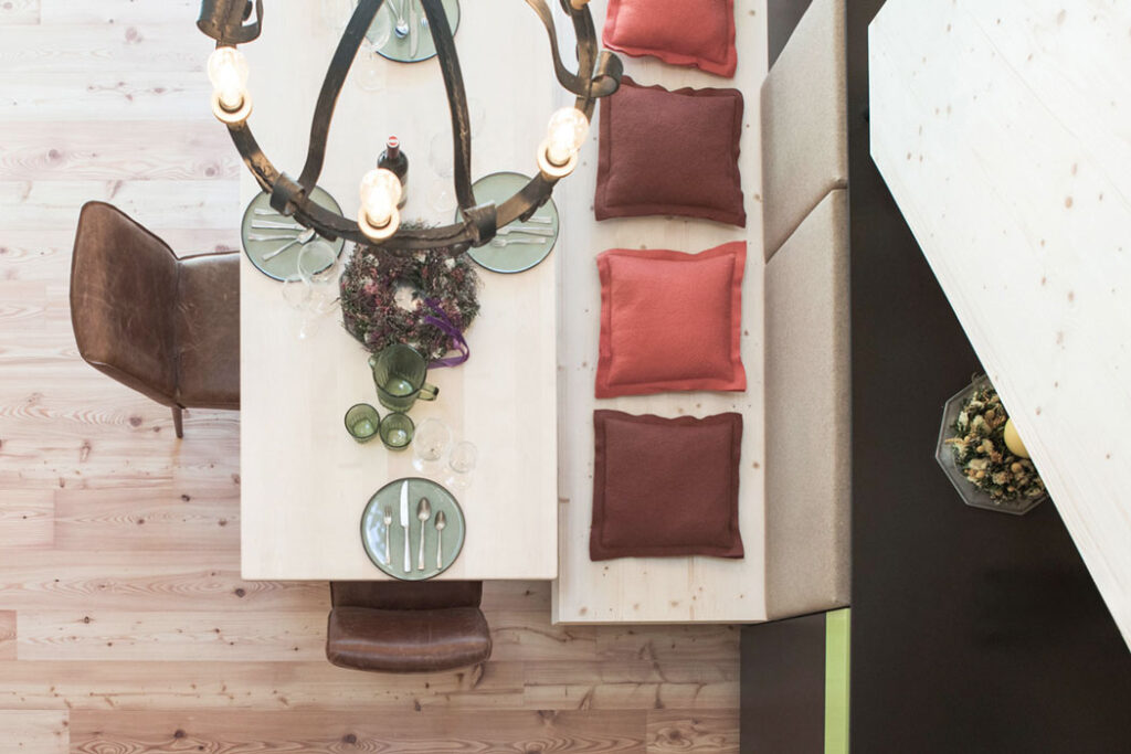 Draufsicht auf einen gedeckten Holztisch mit farbigen Kissen, Geschirr und Kronleuchter.