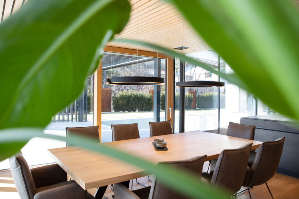 Essbereich mit Holztisch, umrahmt von grünen Pflanzen und viel Tageslicht