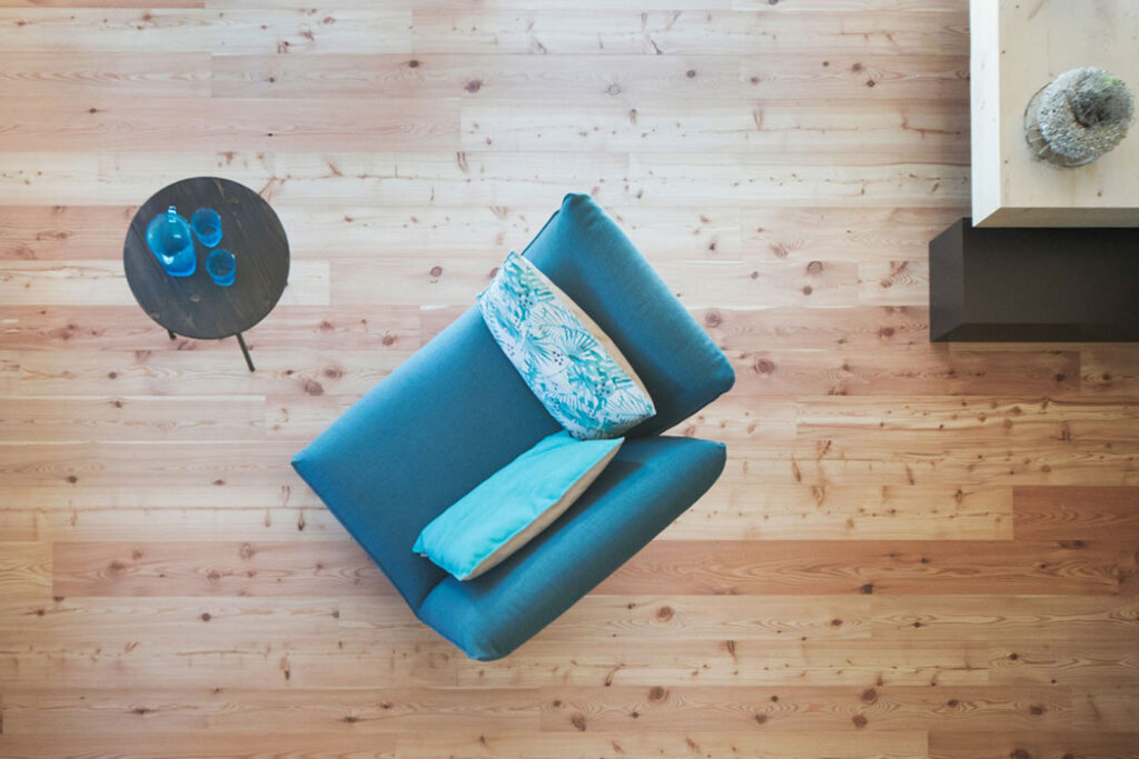 Draufsicht auf blauen Sessel mit Kissen auf Holzboden, daneben ein kleiner Beistelltisch.