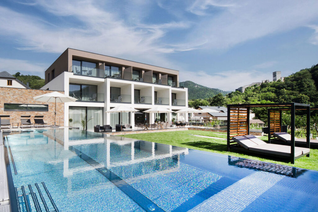 Modernes Hotel mit großen Glasfronten und Infinity-Pool, klare Linien in alpiner Landschaft.