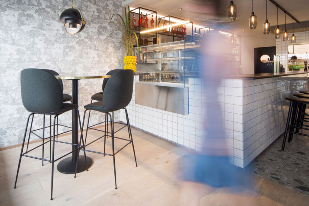 Innenaufnahme eines modernen Gastronomie-Konzepts mit Barhockern, Fliesen und Bewegungsunschärfe.