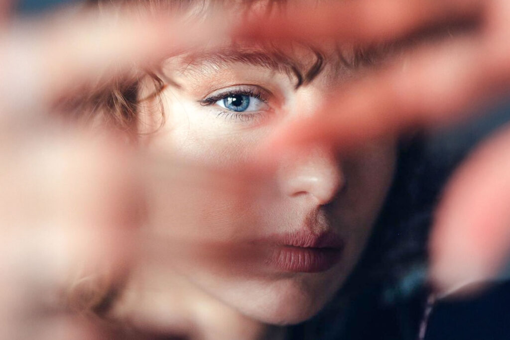 Porträt einer Frau mit blauem Auge, teilweise durch eine verschwommene Hand verdeckt.
