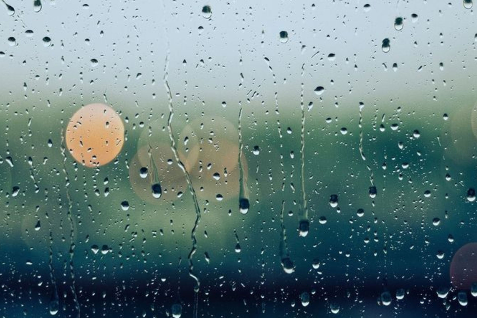 Regentropfen auf einer Fensterscheibe mit unscharfer Landschaft im Hintergrund.