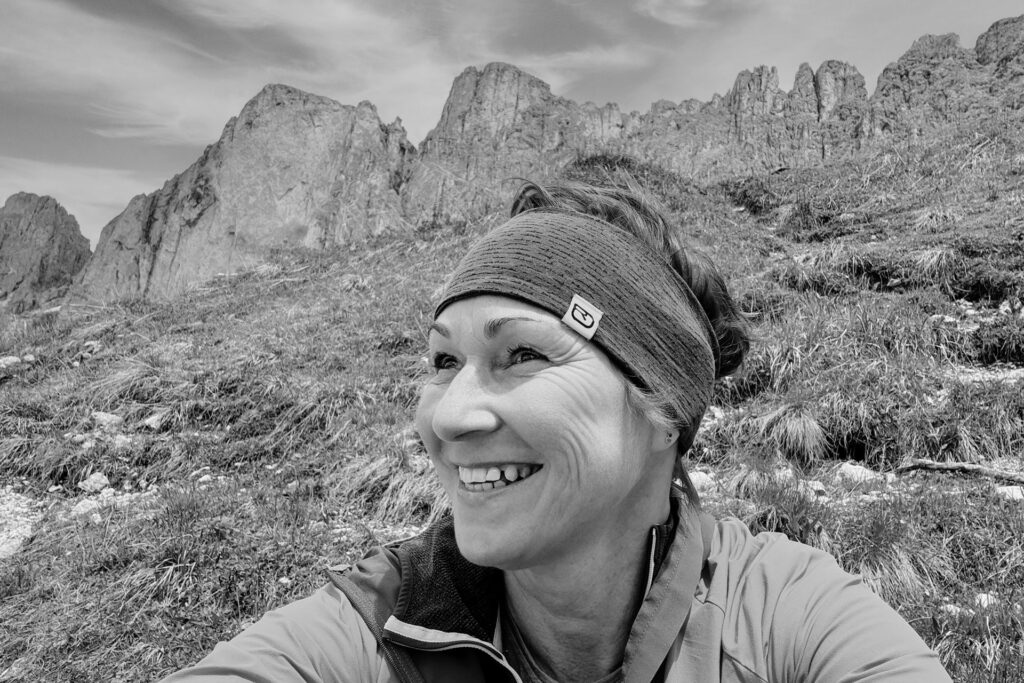 Schwarz-weiß-Aufnahme einer Frau mit Kurzhaarschnitt, die eine Kamera hält und freundlich lächelt – offen, professionell, authentisch.