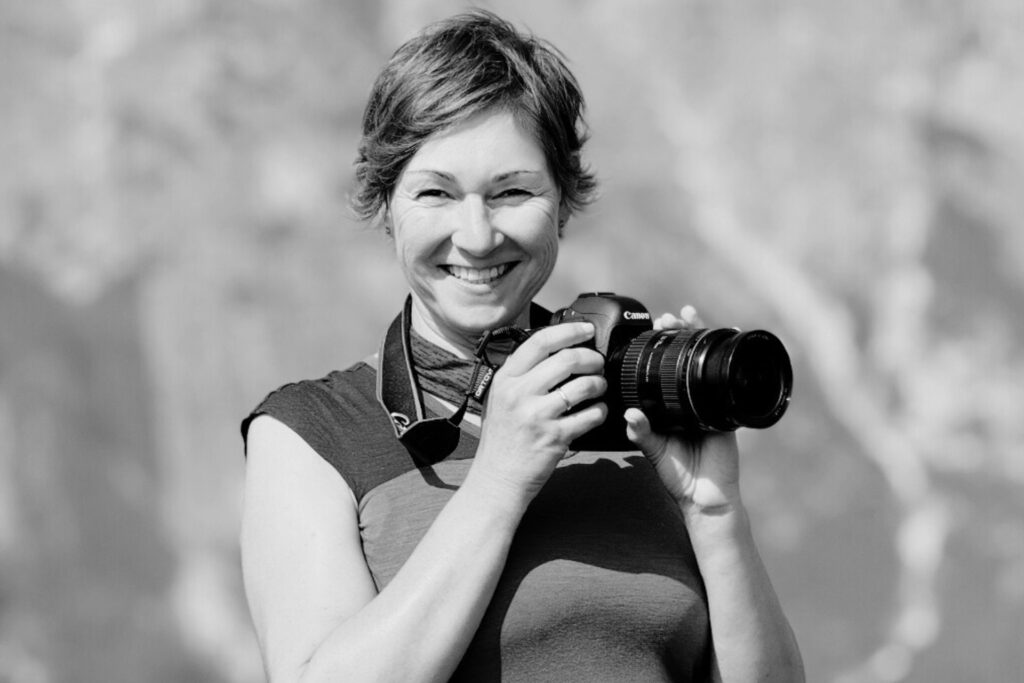 Frau mit Kamera lächelt in die Kamera