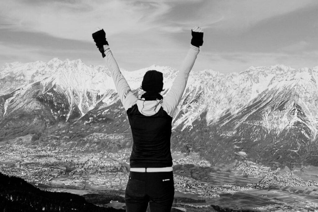 Frau mit erhobenen Armen vor verschneiten Bergen