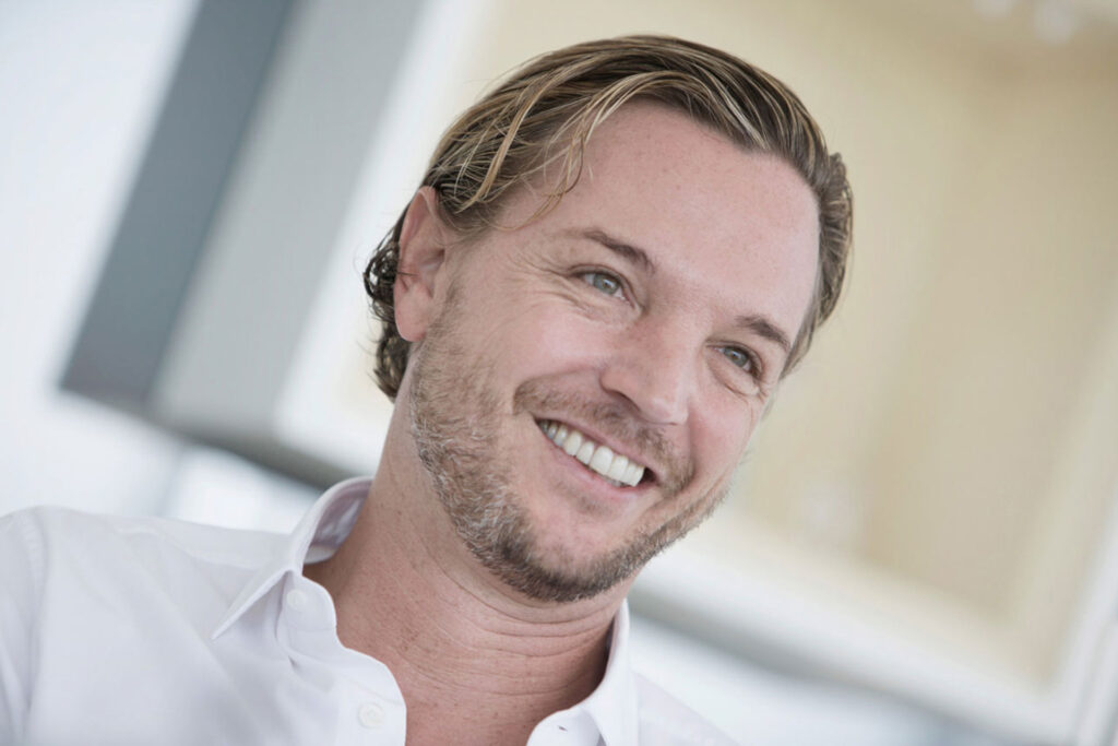 Lächelnder Mann mit offenem Hemd im Porträt.