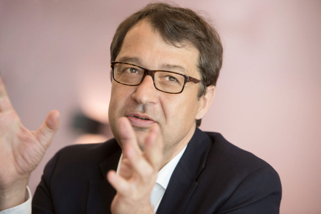 Porträt eines Mannes mit Brille in Anzug und Hemd, spricht und gestikuliert.