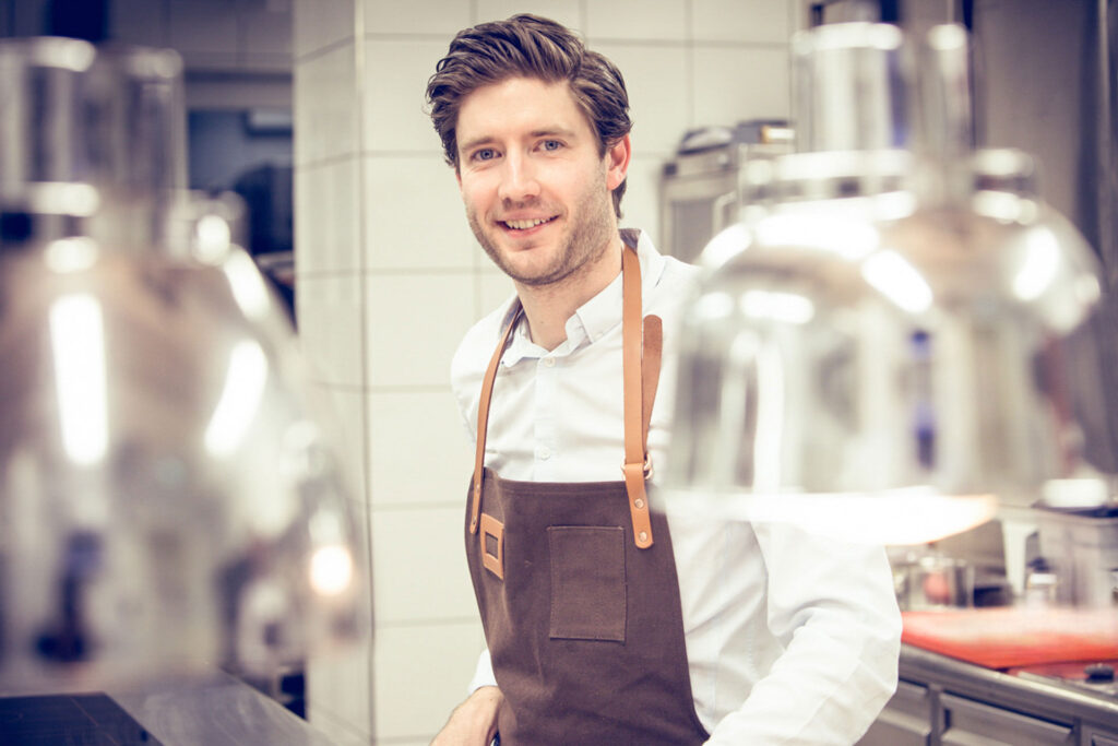 Porträt eines Kochs mit Schürze in einer Profiküche.