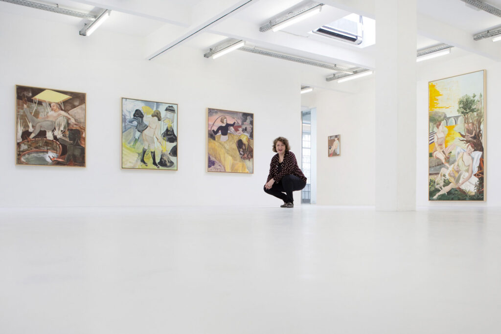Frau in Galerie mit großem Weißraum und farbigen Gemälden an der Wand.