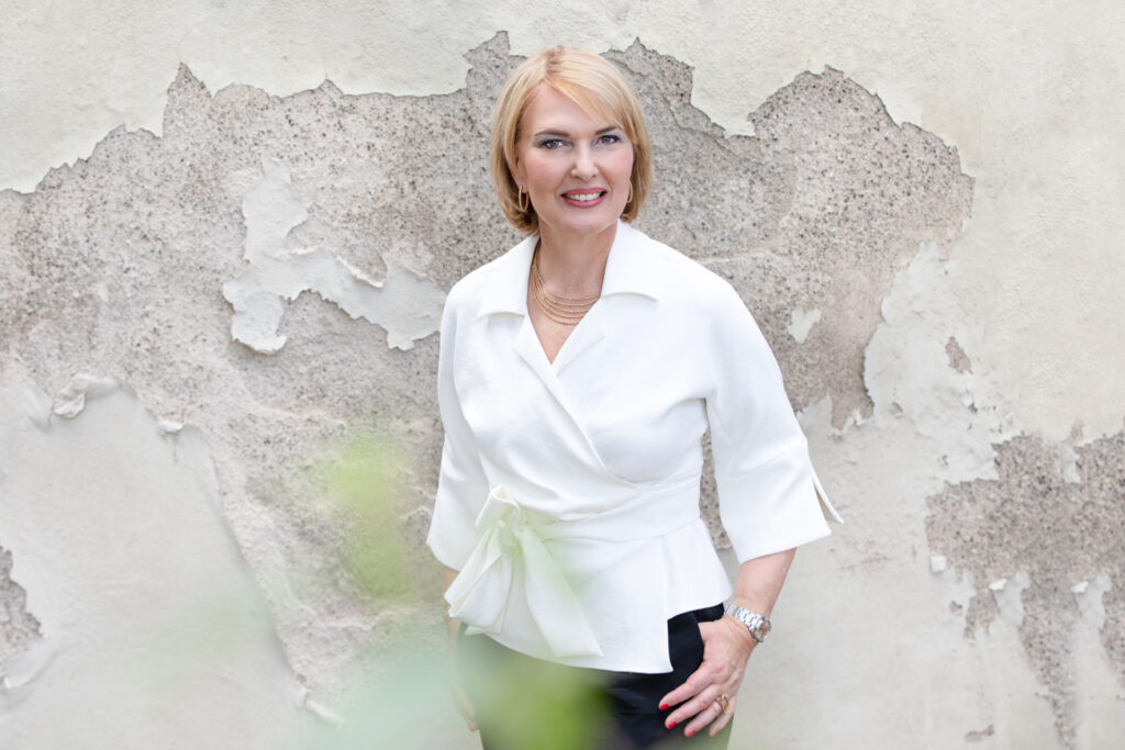 Frau in weißer Bluse vor verwitterter Wand.