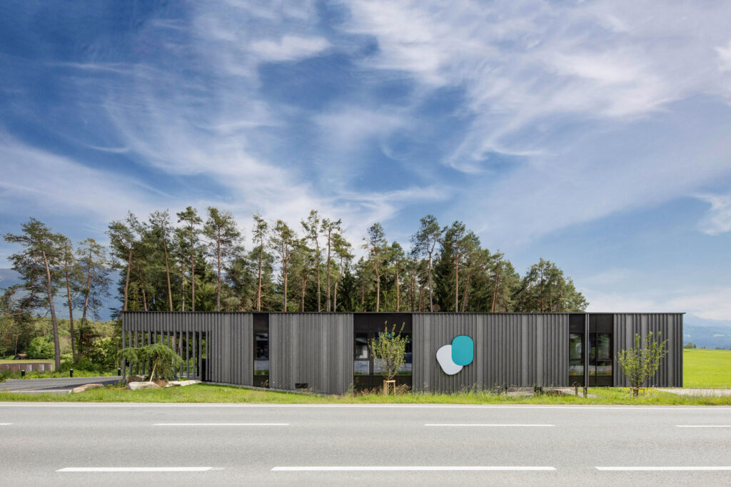 Moderne Praxis Dr. Oberleit mit dunkler Fassade und großem Logo, eingebettet in eine grüne Waldkulisse.