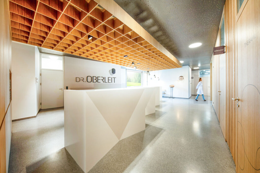 Moderner Empfangsbereich in der Praxis Dr. Oberleit mit weißem Tresen, Holzdecke und heller Atmosphäre.